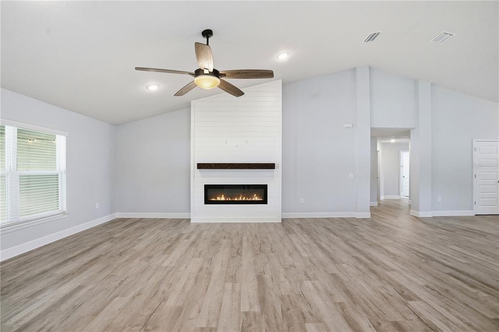 A living room features light gray walls, wood-look flooring, a ceiling fan, and a fireplace — 12847 HILARY STREET, SPRING HILL, FL
