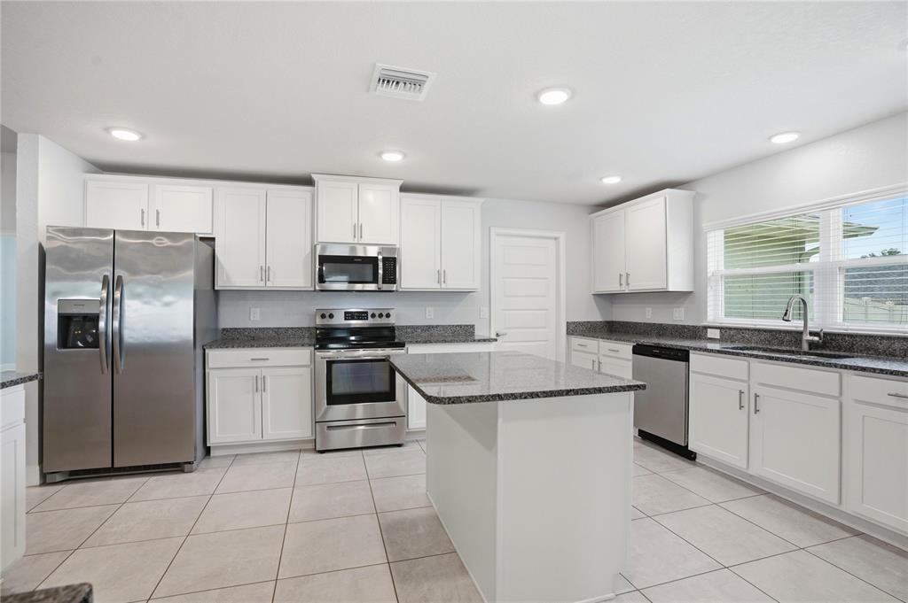A kitchen features white cabinets, granite countertops, stainless steel appliances, and a central island — 12847 HILARY STREET, SPRING HILL, FL