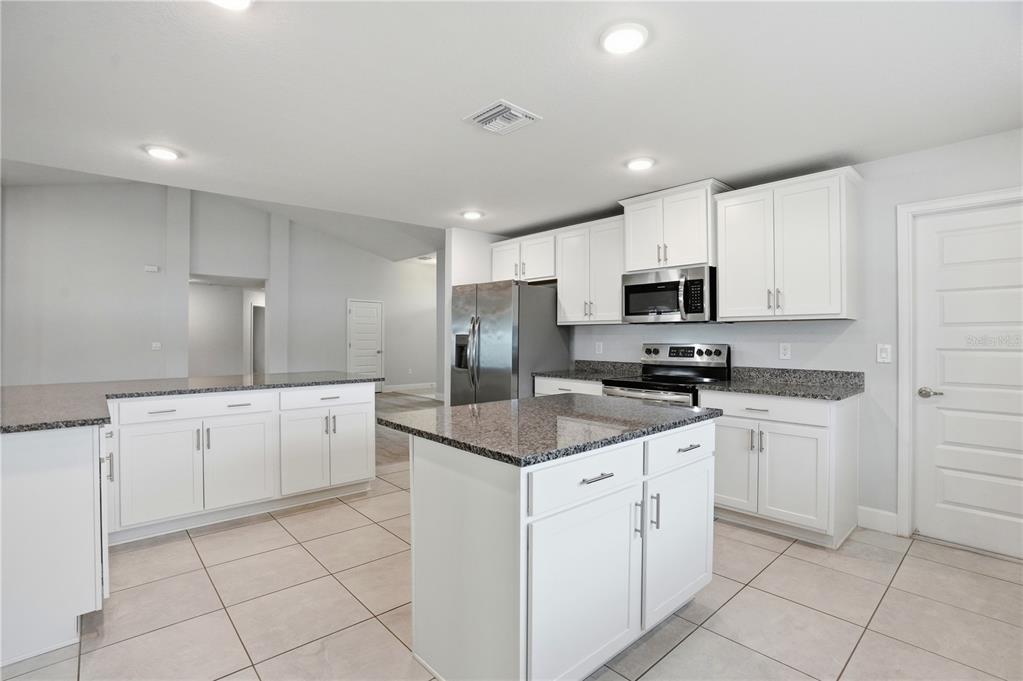 A kitchen features white cabinets, granite countertops, a center island, and stainless steel appliances — 12847 HILARY STREET, SPRING HILL, FL