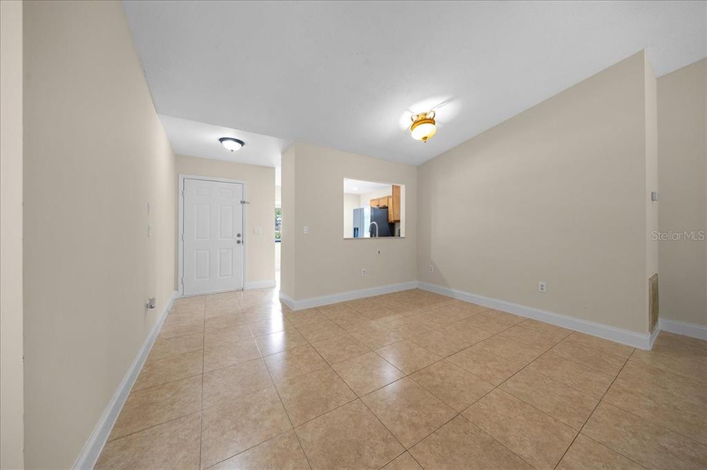 An empty room with beige walls, tile flooring, a ceiling light, and a kitchen pass-through — 5059 SW 196TH AVENUE, DUNNELLON, FL