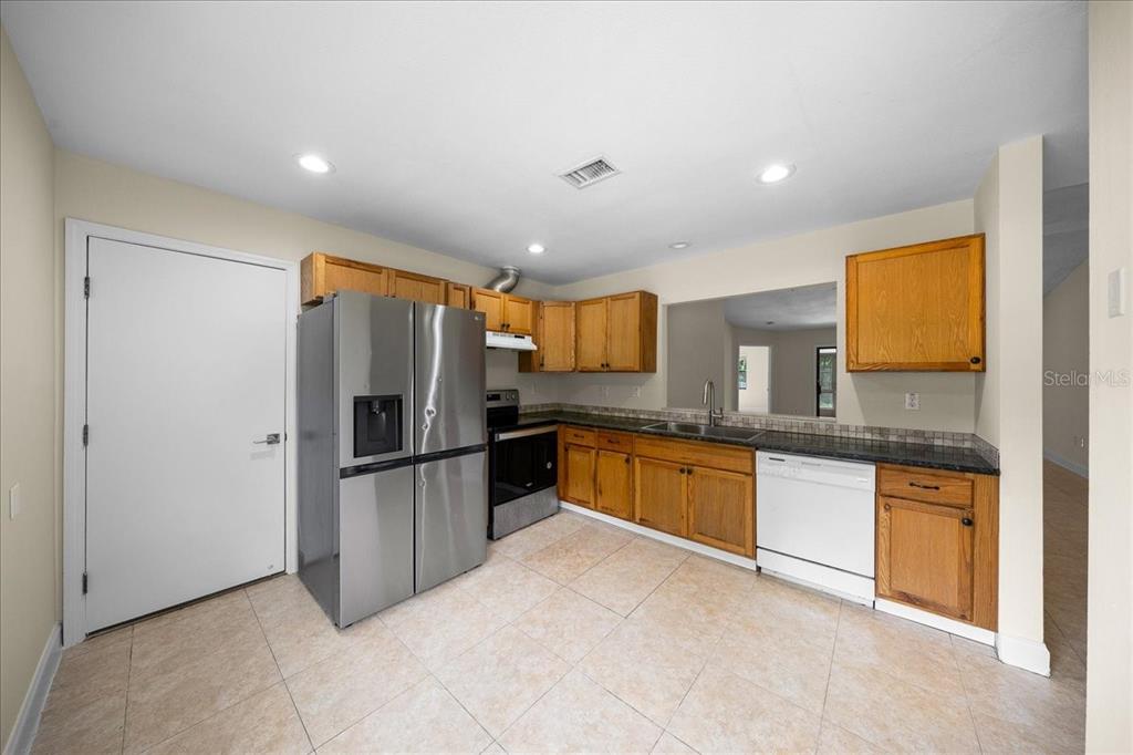 A kitchen features light tile flooring, wood cabinets, stainless steel appliances, and a white dishwasher — 5059 SW 196TH AVENUE, DUNNELLON, FL