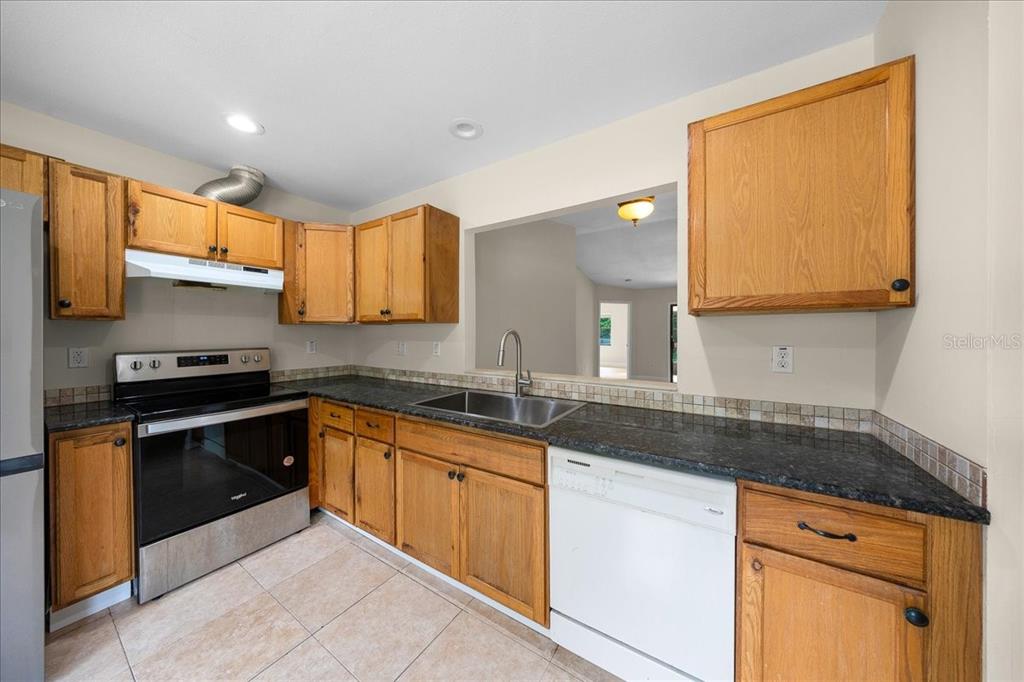 A kitchen features wood cabinets, dark granite countertops, stainless steel appliances, and tile flooring — 5059 SW 196TH AVENUE, DUNNELLON, FL