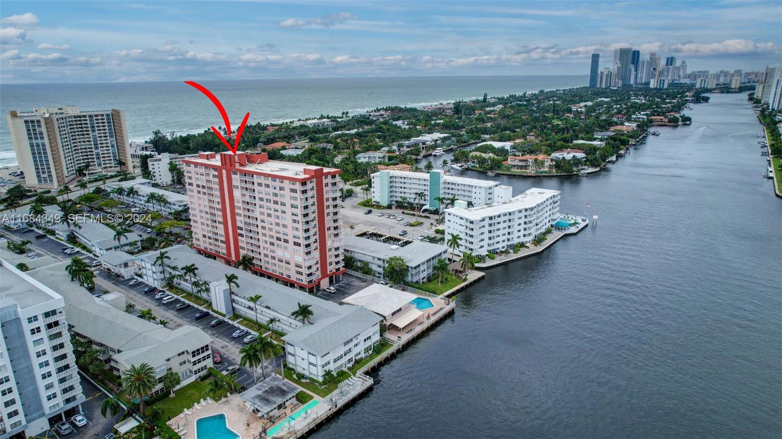 An aerial view shows a tall, salmon-colored apartment building near a waterway and ocean — 3161 S Ocean Dr # 203, Hallandale Beach FL 33009, HALLANDALE BEACH, FL