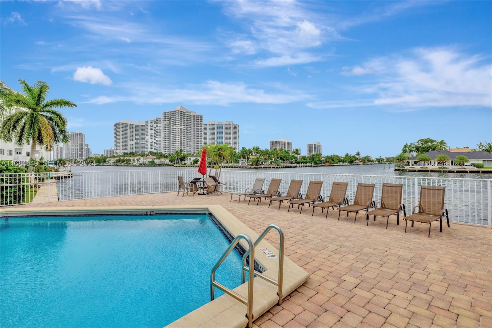 A swimming pool with lounge chairs sits on a paved deck overlooking a waterway — 3161 S Ocean Dr # 203, Hallandale Beach FL 33009, HALLANDALE BEACH, FL