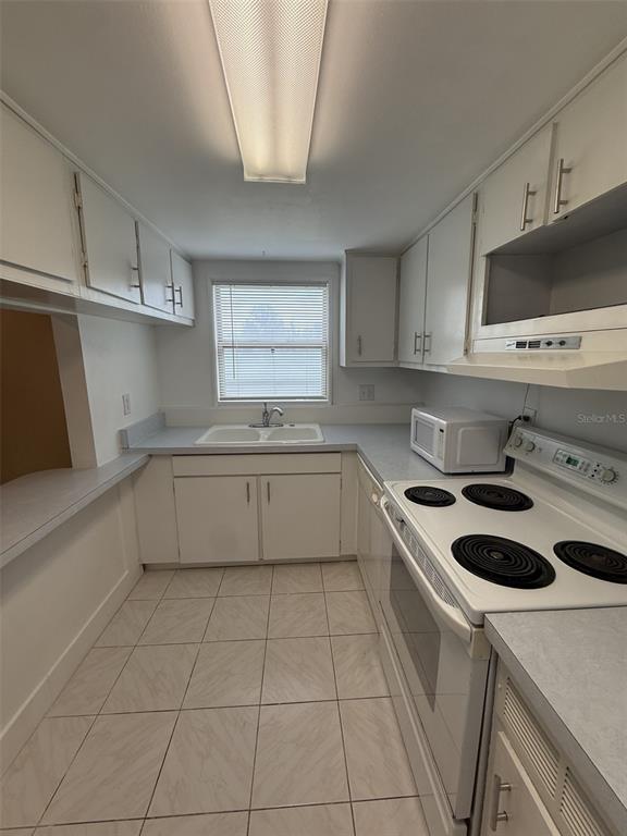 A galley kitchen features white cabinets, light countertops, a white electric range, and tiled flooring — 7701 STARKEY ROAD UNIT 239, SEMINOLE, FL