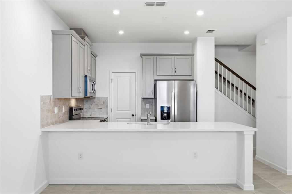 A modern kitchen features gray cabinets, stainless steel appliances, white countertops, and a breakfast bar — 10047 GAZEBO ALLEY, ORLANDO, FL