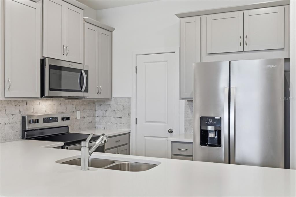 A kitchen features gray cabinets, stainless steel appliances, a white countertop, and a tiled backsplash — 10047 GAZEBO ALLEY, ORLANDO, FL