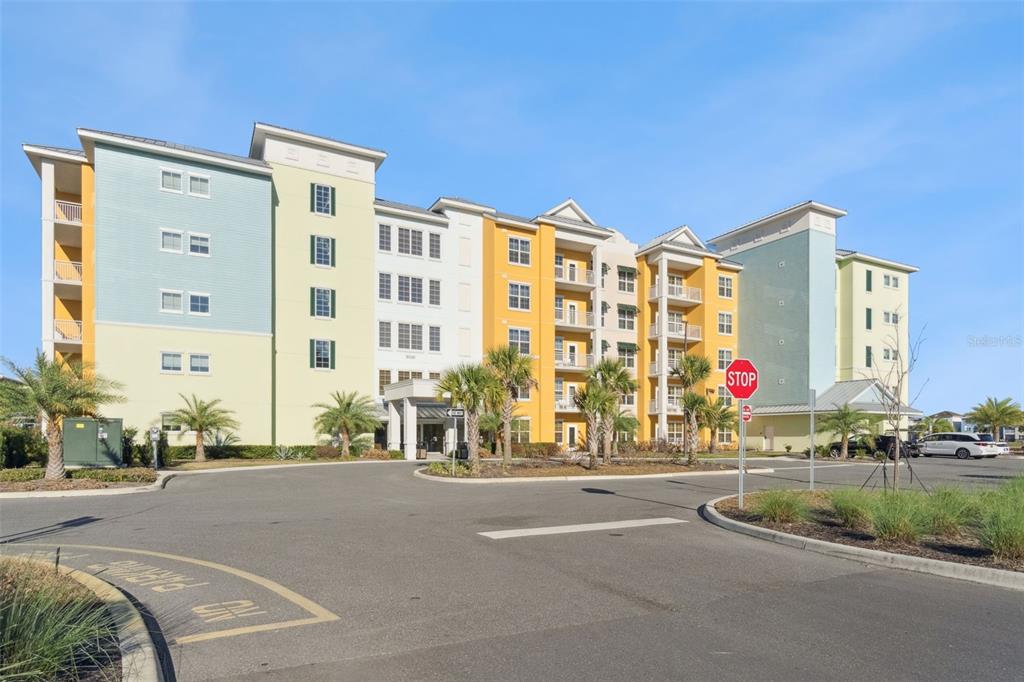 A multi-story apartment building with colorful exterior walls stands behind a paved parking lot — 8061 VACATION AVENUE UNIT 2510, KISSIMMEE, FL