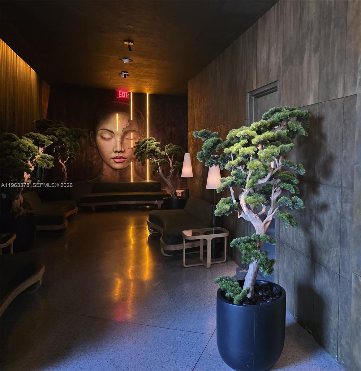 A dimly lit lounge features dark walls, potted bonsai trees, modern seating, and a mural — 159 NE 6th St # 4302, Miami FL 33132, MIAMI, FL