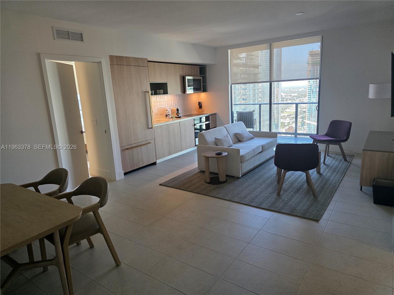 An open-concept living area features a kitchen with light wood cabinetry and floor-to-ceiling windows — 159 NE 6th St # 4302, Miami FL 33132, MIAMI, FL
