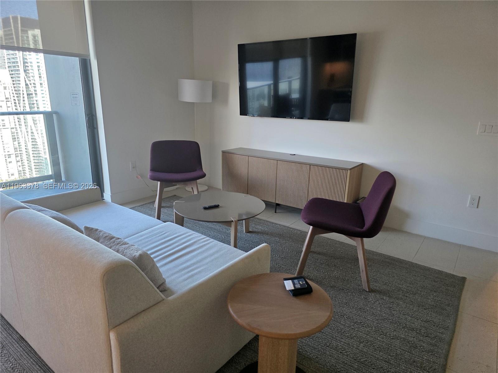 A modern living room features a sofa, two purple chairs, a television, and a balcony — 159 NE 6th St # 4302, Miami FL 33132, MIAMI, FL
