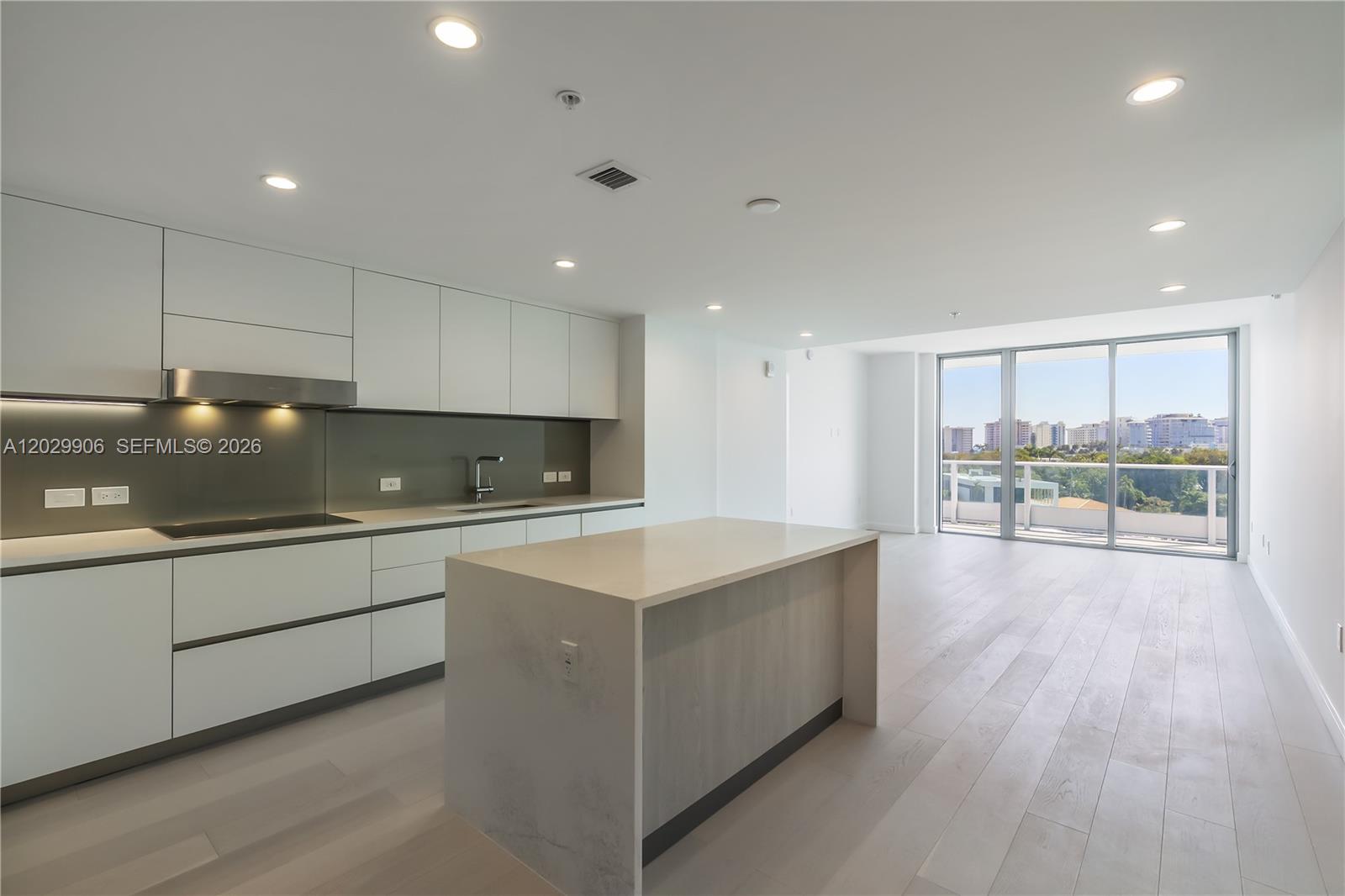 A modern kitchen features white cabinetry, a central island, and a balcony with city views — 9201 E Bay Harbor Dr # 603, Bay Harbor Islands FL 33154, BAY HARBOR ISLANDS, FL