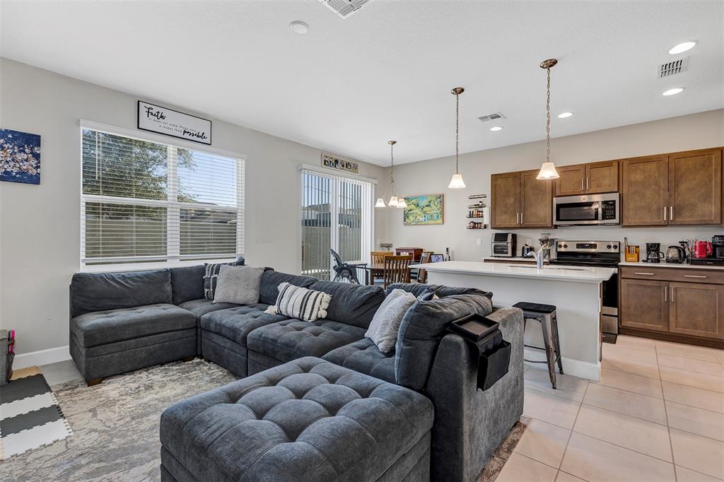An open-concept living room and kitchen featuring a large sectional sofa and wooden cabinets — 1401 CAPTIVA COVE UNIT 23, SANFORD, FL