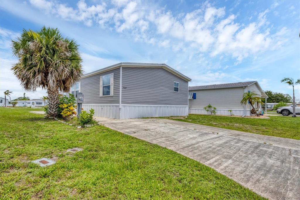 A gray manufactured home with a concrete driveway and a palm tree in the yard — 7337 DESANT LANE, PORT CHARLOTTE, FL