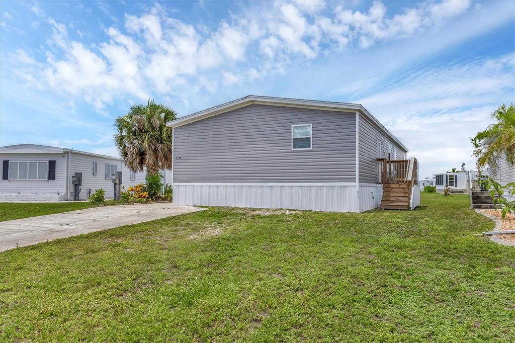 A gray manufactured home with a concrete driveway and a small wooden staircase on the side — 7337 DESANT LANE, PORT CHARLOTTE, FL