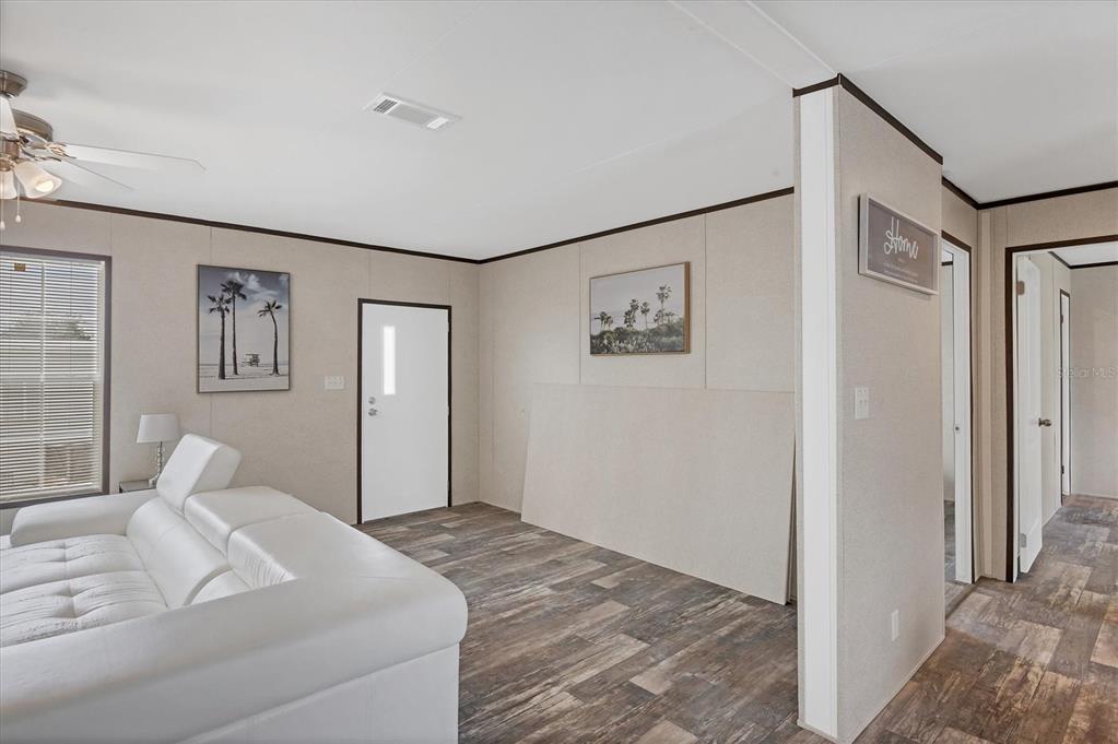 A living room with light-colored walls, wood-look flooring, a white sofa, and a white door — 7337 DESANT LANE, PORT CHARLOTTE, FL