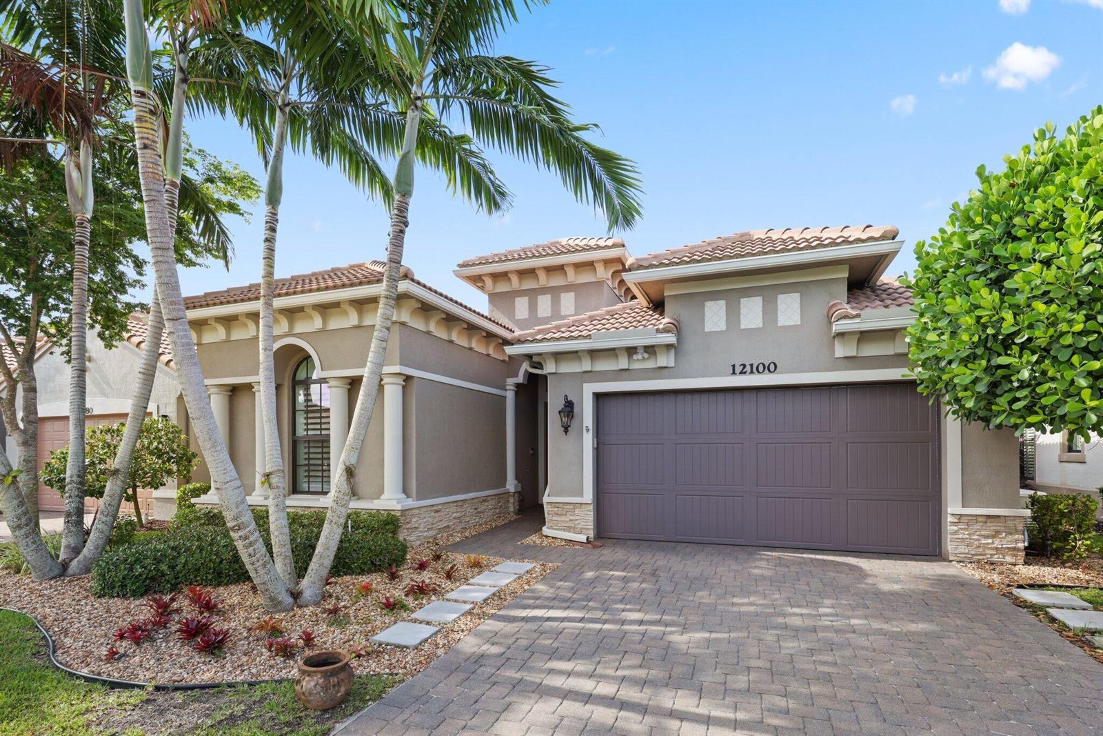 A single-story house with a brown garage door, stone accents, and palm trees in front — 12100 Kalmar Circle S, Parkland FL 33076, PARKLAND, FL