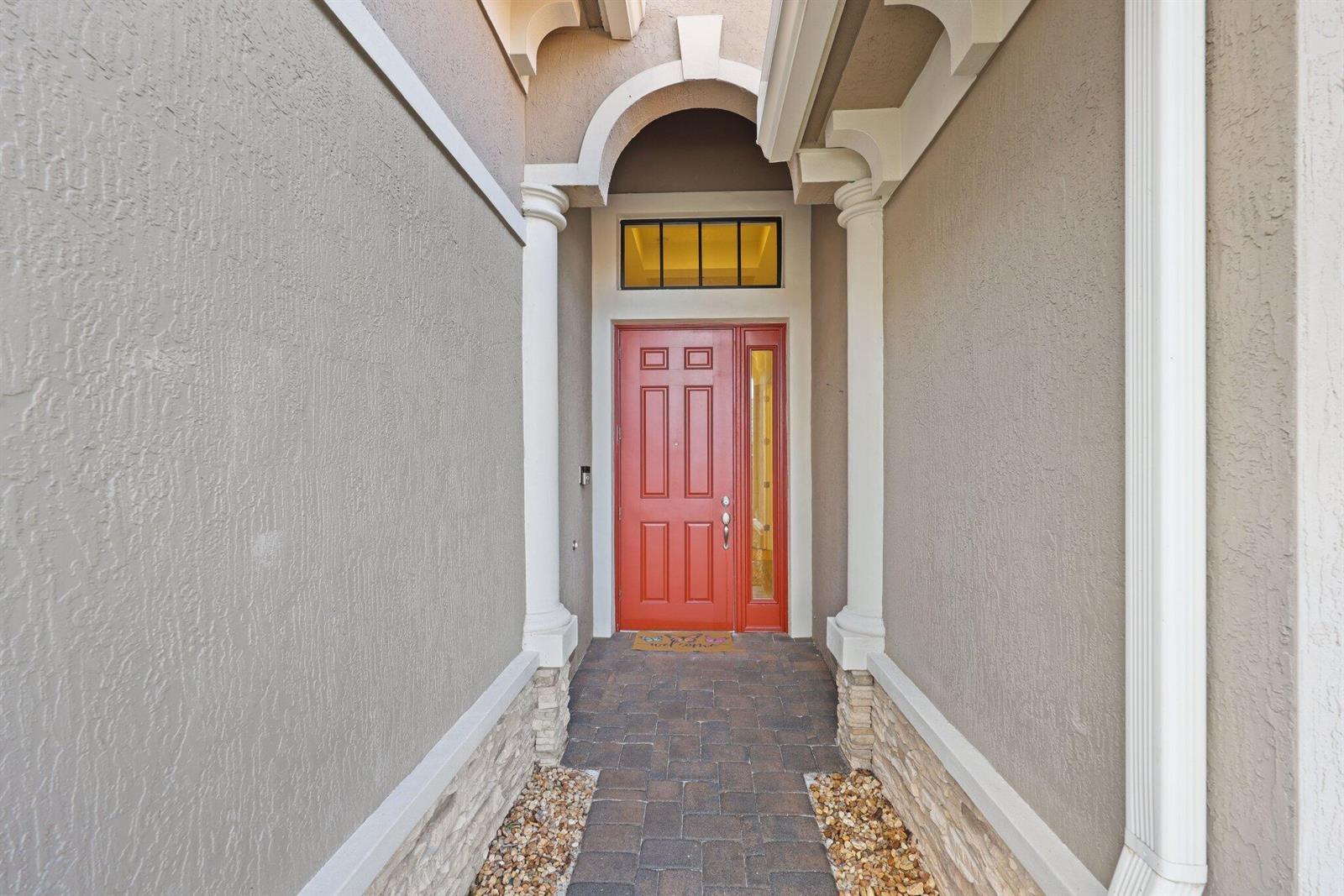A red front door is framed by white columns and stone accents in an entryway — 12100 Kalmar Circle S, Parkland FL 33076, PARKLAND, FL