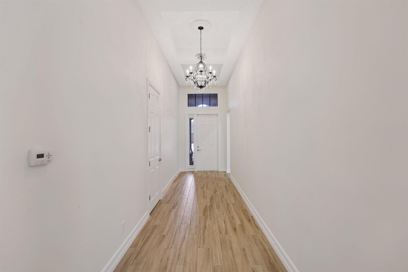 A bright entryway features wood-look tile flooring, a crystal chandelier, and a white front door — 12100 Kalmar Circle S, Parkland FL 33076, PARKLAND, FL