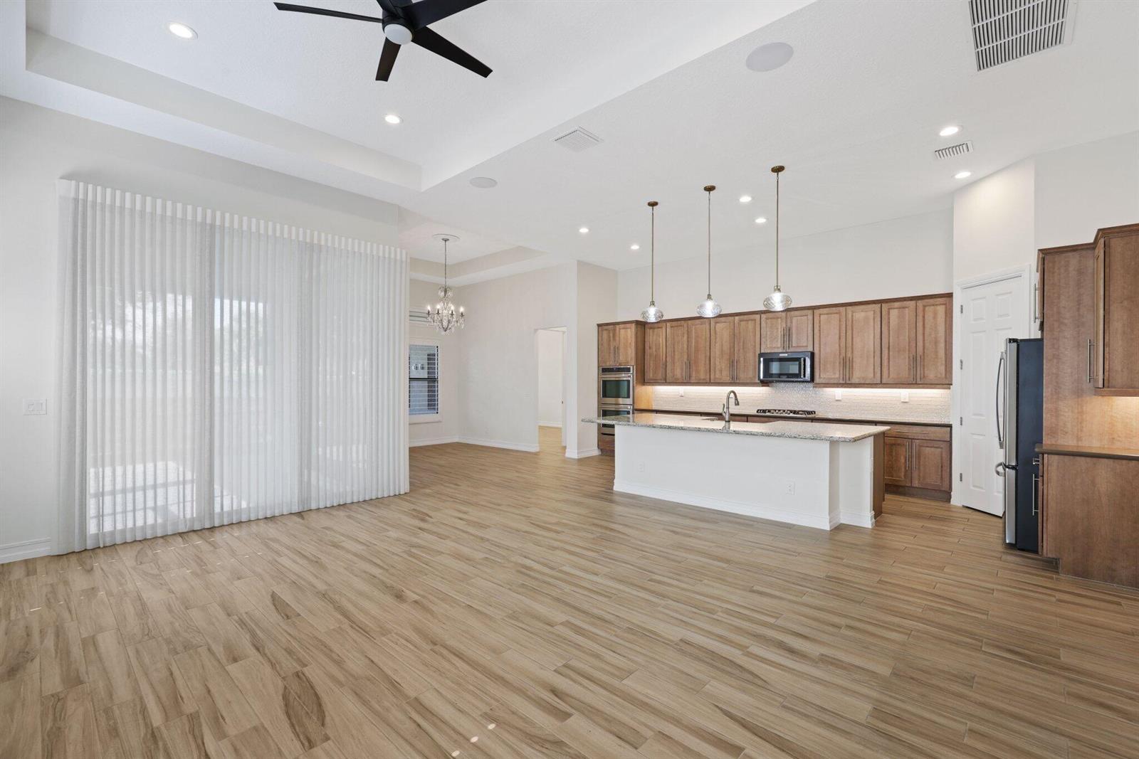 An open-concept kitchen and living area features wood-look tile flooring, white cabinetry, and pendant lighting — 12100 Kalmar Circle S, Parkland FL 33076, PARKLAND, FL