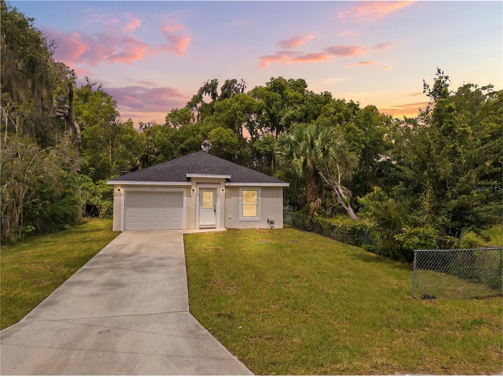 A single-story house with a concrete driveway, a garage, and a lawn under a sunset sky — 312 ALBANY AVENUE, DELAND, FL
