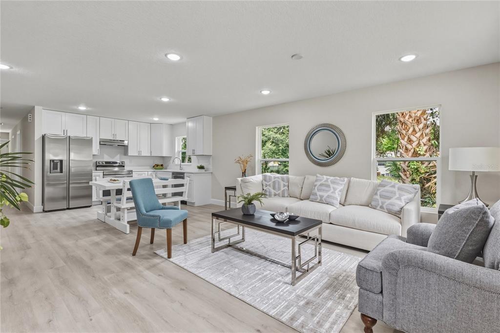 An open-concept living room and kitchen featuring white cabinetry, light wood flooring, and neutral furniture — 312 ALBANY AVENUE, DELAND, FL