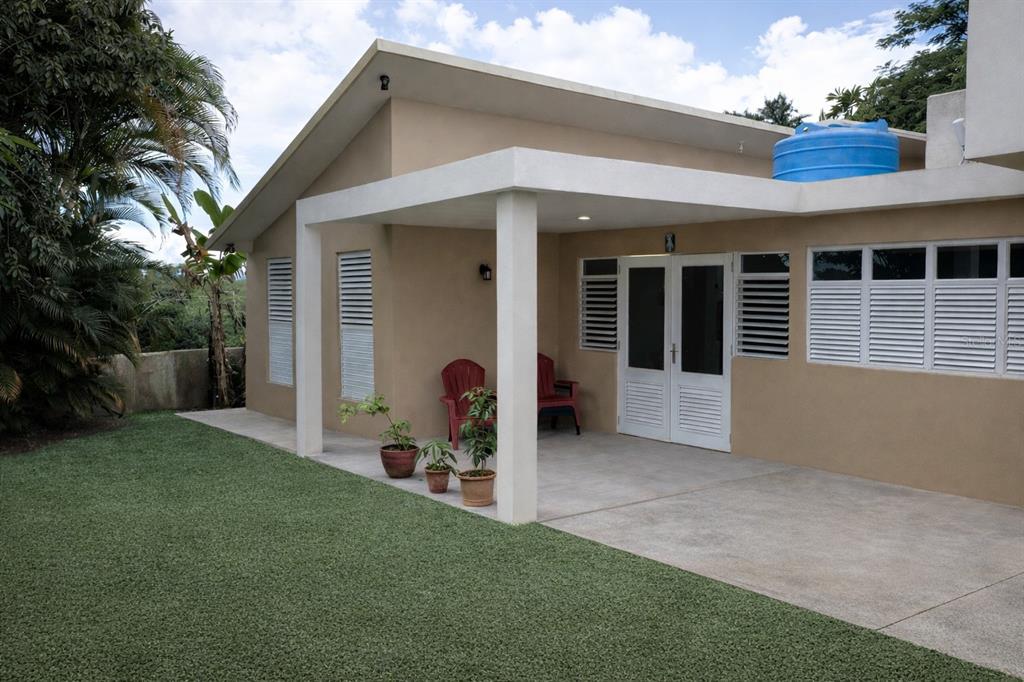 A tan house exterior features a covered concrete patio, white shutters, and a blue water tank — Carr 793 KM 1.2 QUINTAS DE JAGUEYES 31A, AGUAS BUENAS, PR