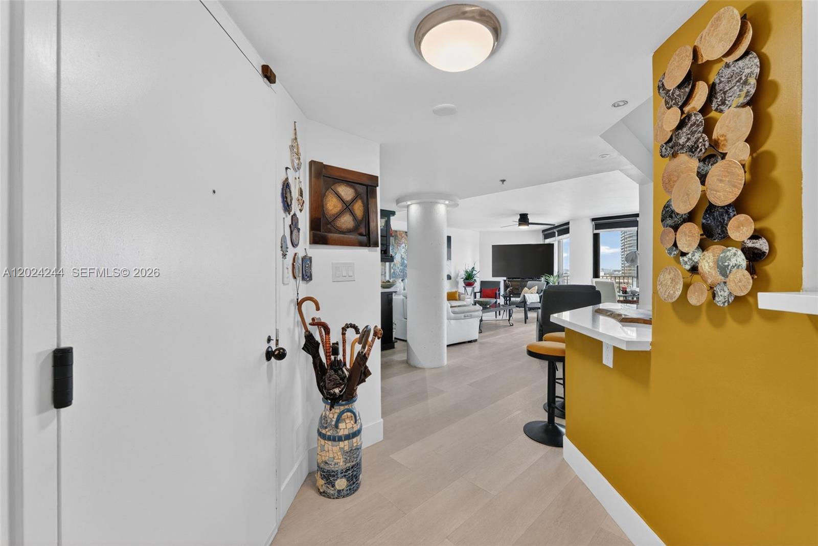 A hallway with light wood flooring leads into an open-concept living area with a pillar — 300 Three Islands Blvd # 710, Hallandale Beach FL 33009, HALLANDALE BEACH, FL