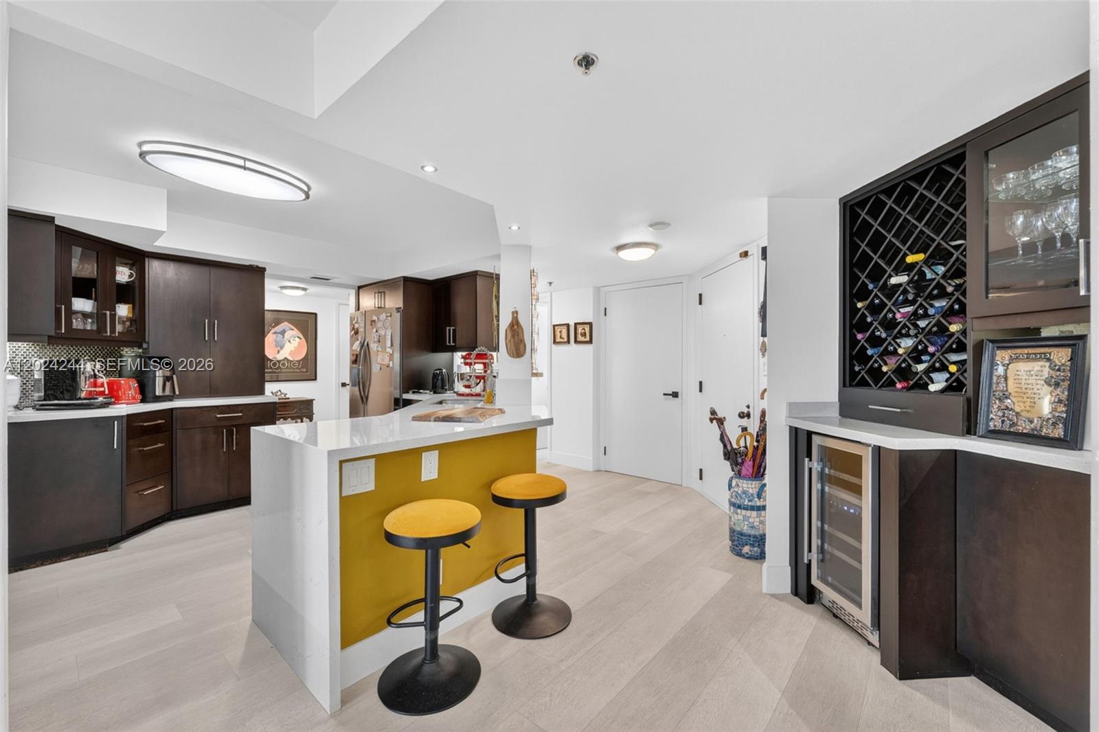 A kitchen features dark wood cabinetry, a yellow island with bar stools, and a wine cooler — 300 Three Islands Blvd # 710, Hallandale Beach FL 33009, HALLANDALE BEACH, FL