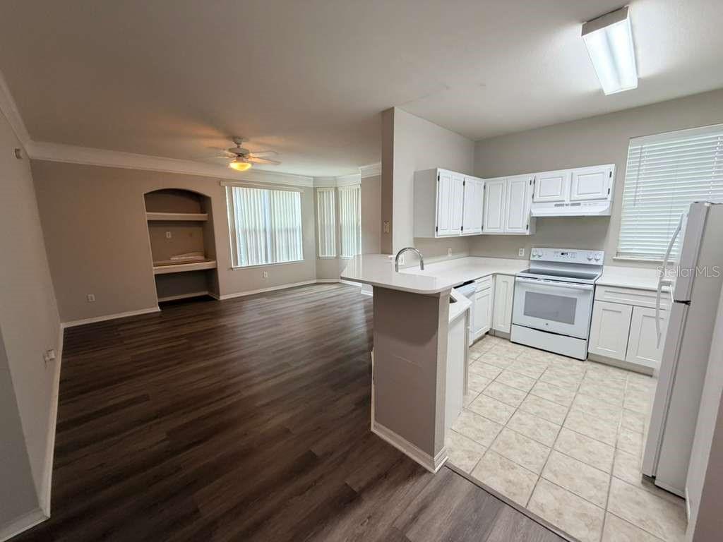 A kitchen with white cabinets and tile flooring opens to a living area with wood floors — 3392 WESTCHESTER SQUARE BOULEVARD UNIT 101, ORLANDO, FL