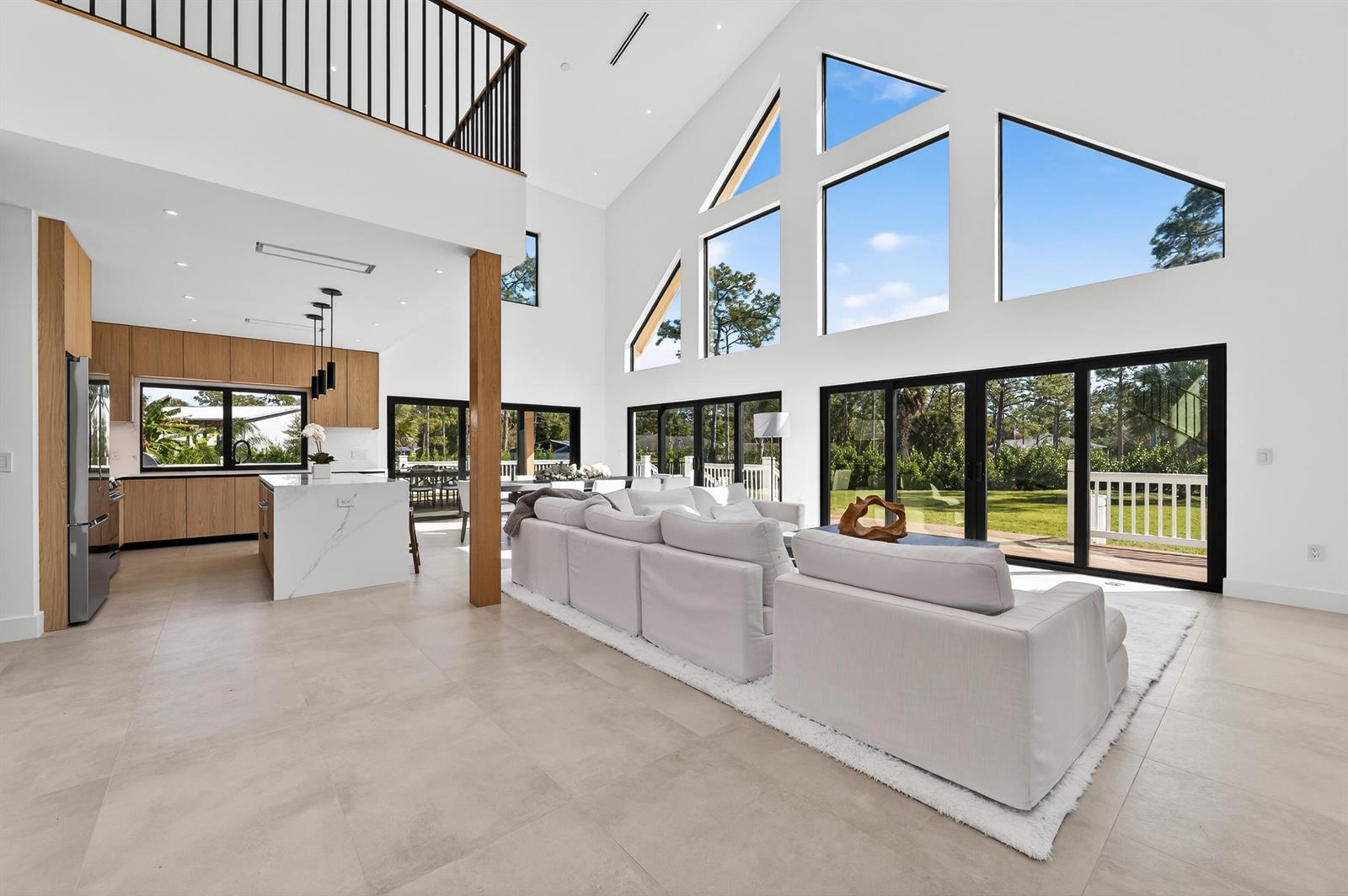A bright, open-concept living room and kitchen featuring high ceilings, large windows, and light flooring — 13613 157th Court N, Jupiter FL 33478, JUPITER, FL