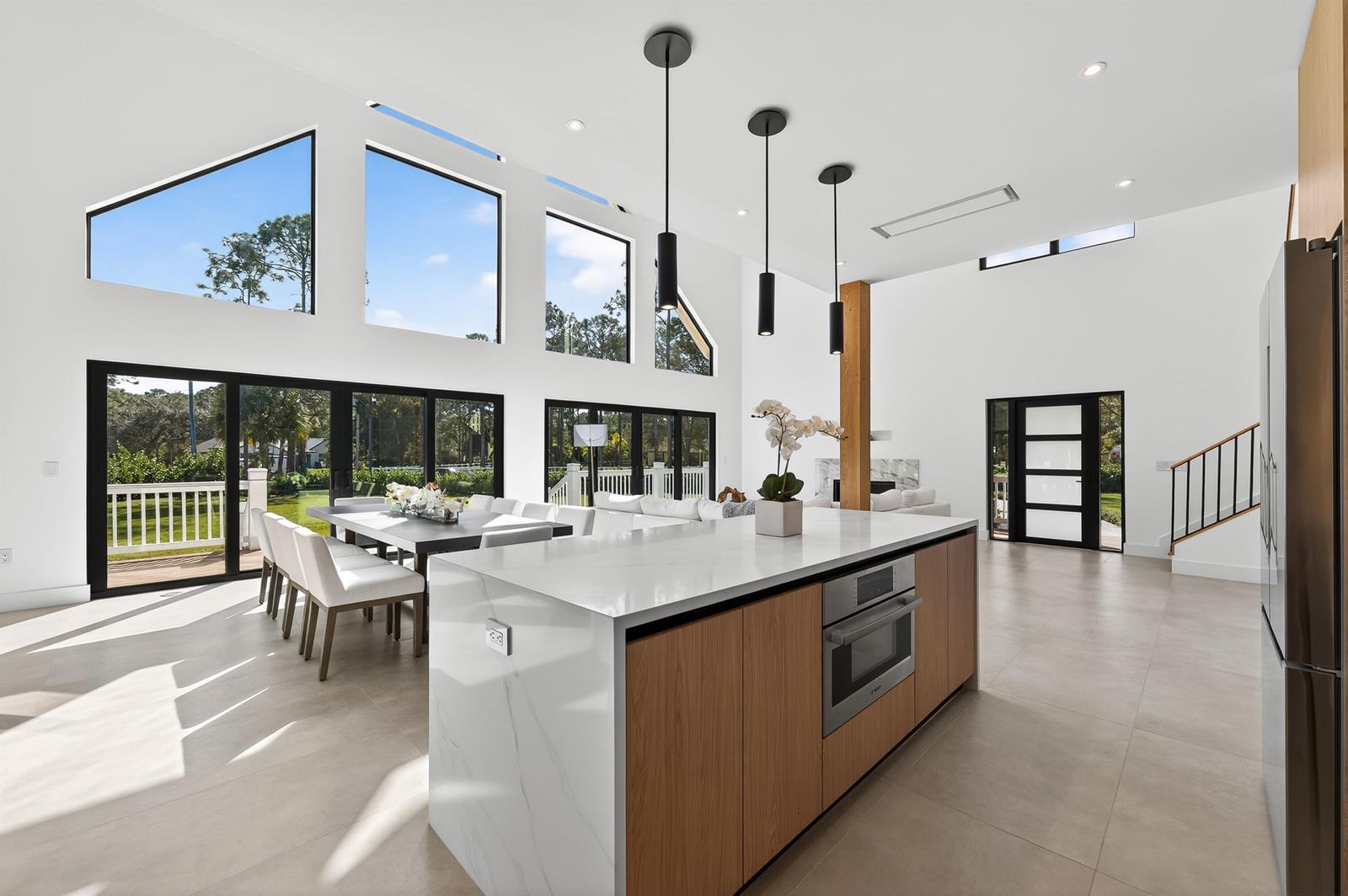 A modern kitchen with a waterfall island, wood cabinetry, and floor-to-ceiling windows overlooking a yard — 13613 157th Court N, Jupiter FL 33478, JUPITER, FL