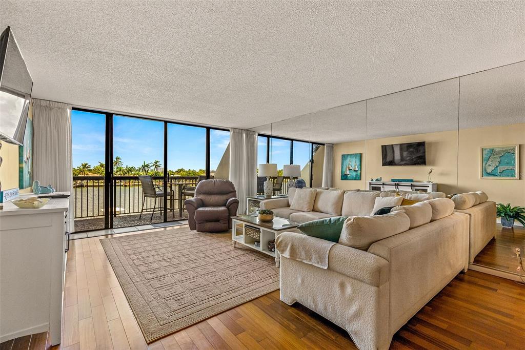 A living room with a large sectional sofa, a recliner, and a balcony overlooking water — 9495 BLIND PASS ROAD UNIT 202, ST PETE BEACH, FL