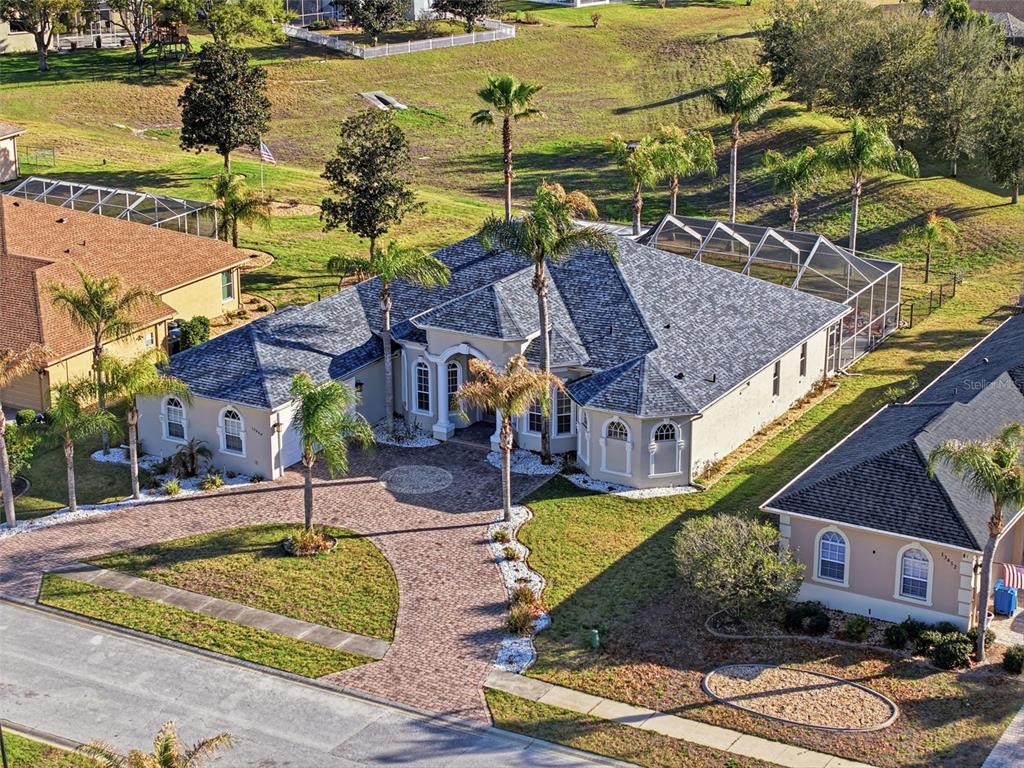 An aerial view of a single-story house with a paver driveway and a screened pool enclosure — 13464 SATINWOOD COURT, SPRING HILL, FL