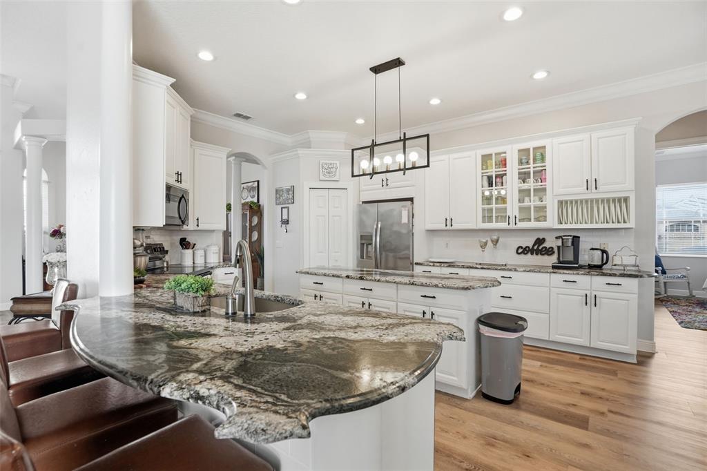 A kitchen features white cabinets, granite countertops, a large island, and wood-look flooring — 13464 SATINWOOD COURT, SPRING HILL, FL