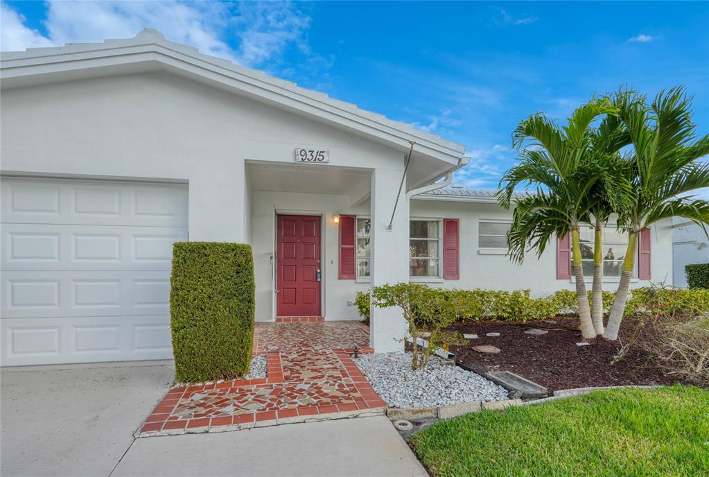 A white house exterior features a red front door, a garage, and a palm tree — 9315 42ND WAY N UNIT #5, PINELLAS PARK, FL