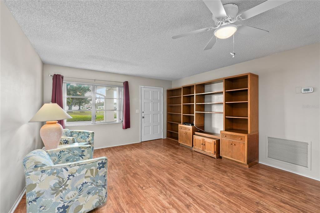 A living room features wood-look flooring, a ceiling fan, built-in shelving, and two floral chairs — 9315 42ND WAY N UNIT #5, PINELLAS PARK, FL