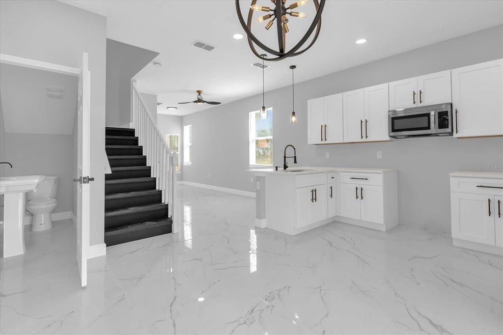 A modern kitchen with white cabinets and marble-look tile floors next to a staircase — 2404 CENTER STREET, SANFORD, FL