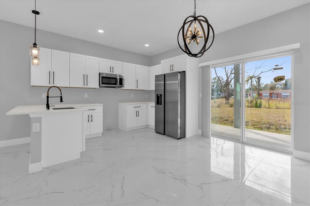 A modern kitchen features white cabinets, stainless steel appliances, and white marble-look tile flooring — 2404 CENTER STREET, SANFORD, FL