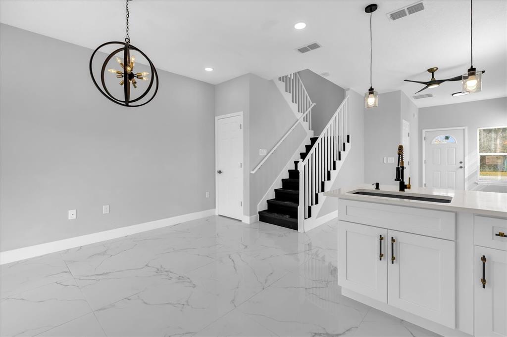 A modern kitchen and dining area featuring white marble-look tile floors and a dark staircase — 2404 CENTER STREET, SANFORD, FL