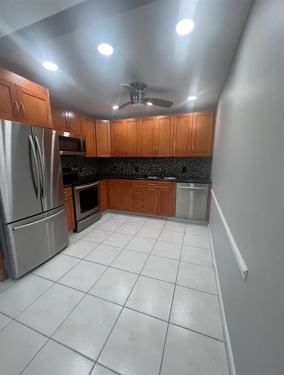 A kitchen features wood cabinets, stainless steel appliances, a dark backsplash, and white tile flooring — 3050 Wolverton C # 3050, Boca Raton FL 33434, BOCA RATON, FL