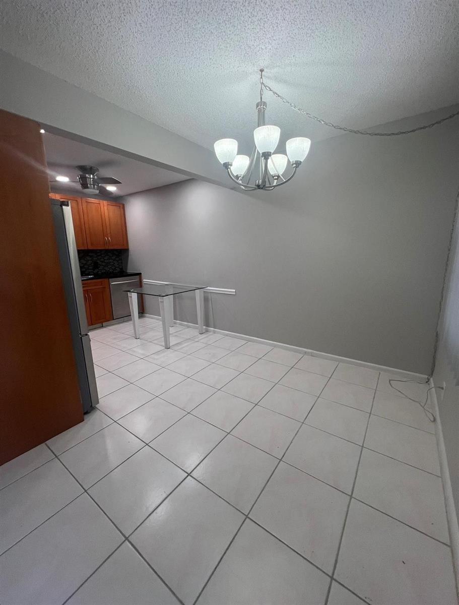 A dining area features white tile floors, a glass table, and a five-light chandelier — 3050 Wolverton C # 3050, Boca Raton FL 33434, BOCA RATON, FL