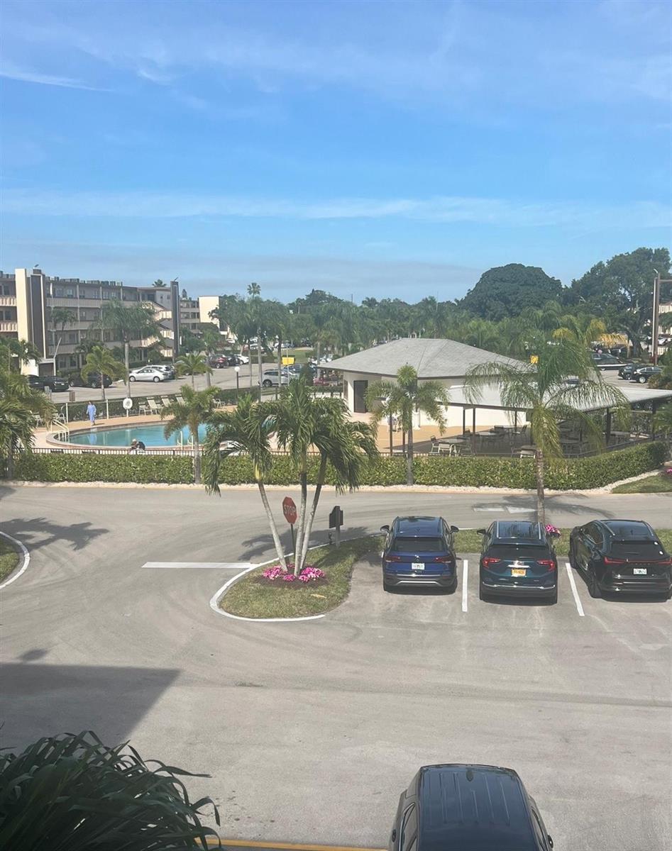 An elevated view of a parking lot, a swimming pool, and a clubhouse with palm trees — 3050 Wolverton C # 3050, Boca Raton FL 33434, BOCA RATON, FL