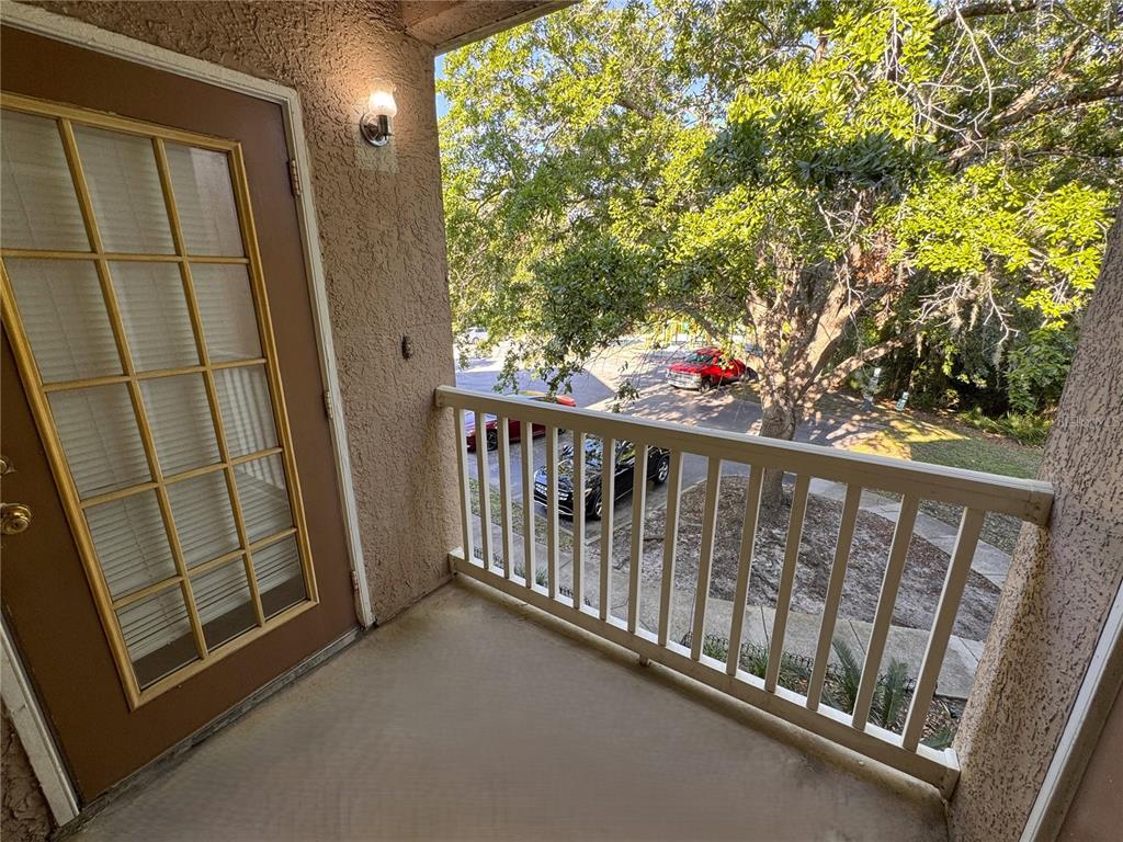 A balcony with a brown door, white railing, and a view of trees and parking — 10519 VILLA VIEW CIRCLE UNIT 10519, TAMPA, FL