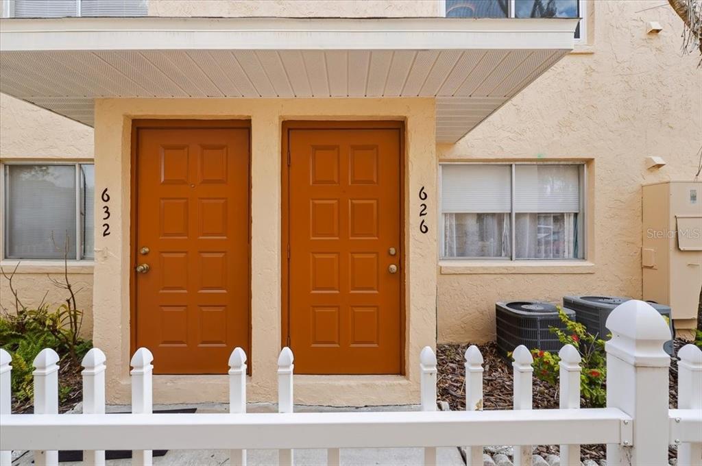Two orange front doors with house numbers are sheltered by a porch under a white fence — 626 PAVARE COURT, WINTER HAVEN, FL