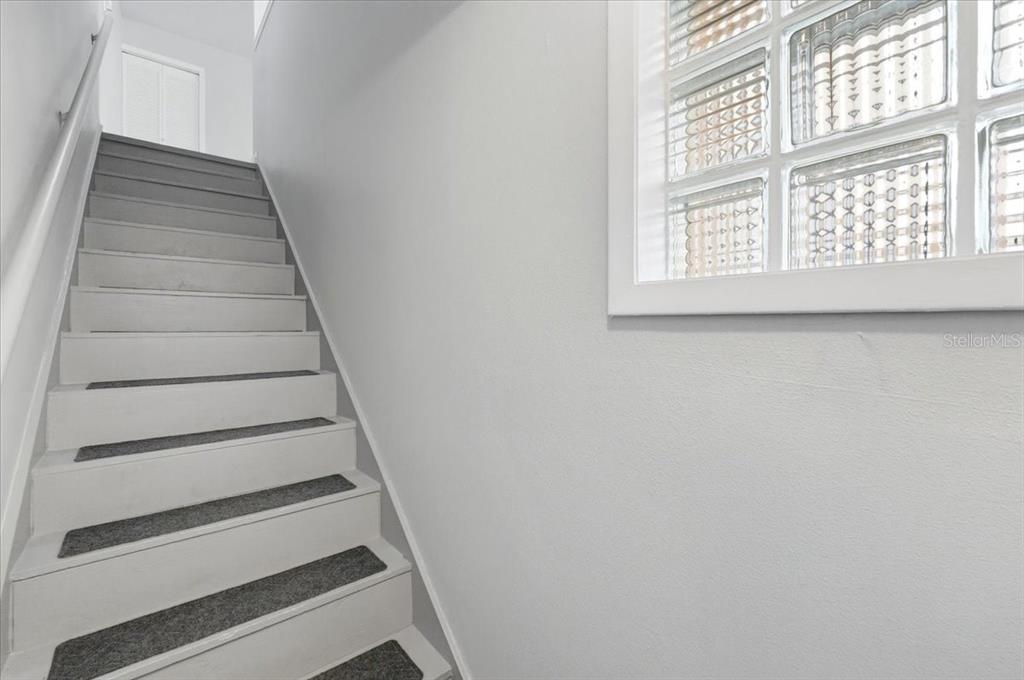 A staircase with white risers and gray treads leads upward beside a glass block window — 626 PAVARE COURT, WINTER HAVEN, FL