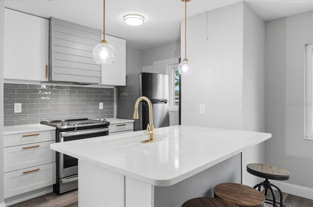 A modern kitchen features white cabinets, a gray tiled backsplash, and a white island — 626 PAVARE COURT, WINTER HAVEN, FL