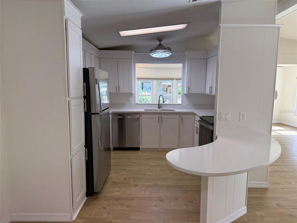 A kitchen features white cabinets, stainless steel appliances, a breakfast bar, and light wood flooring — 130 CLUBVIEW DRIVE UNIT 2, SAFETY HARBOR, FL