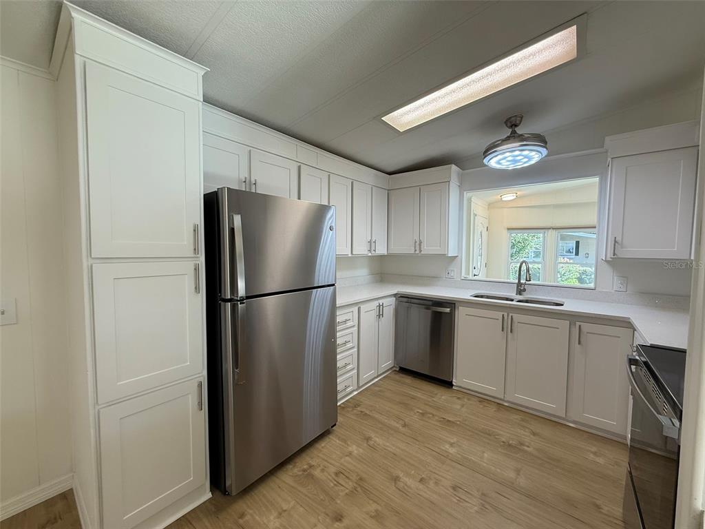A kitchen features white cabinets, stainless steel appliances, and light wood-look flooring — 130 CLUBVIEW DRIVE UNIT 2, SAFETY HARBOR, FL