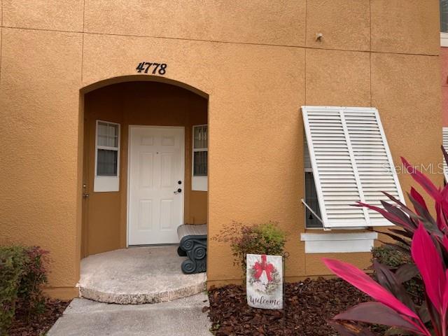 The exterior of a tan stucco building features a recessed entryway with a white door — 4778 VERO BEACH PLACE, KISSIMMEE, FL